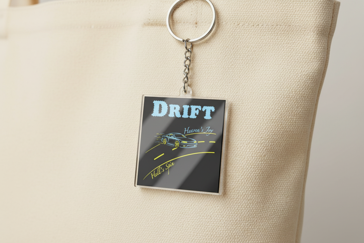 Black square acrylic keychain with applied Drift sticker hanging from a cream tote bag